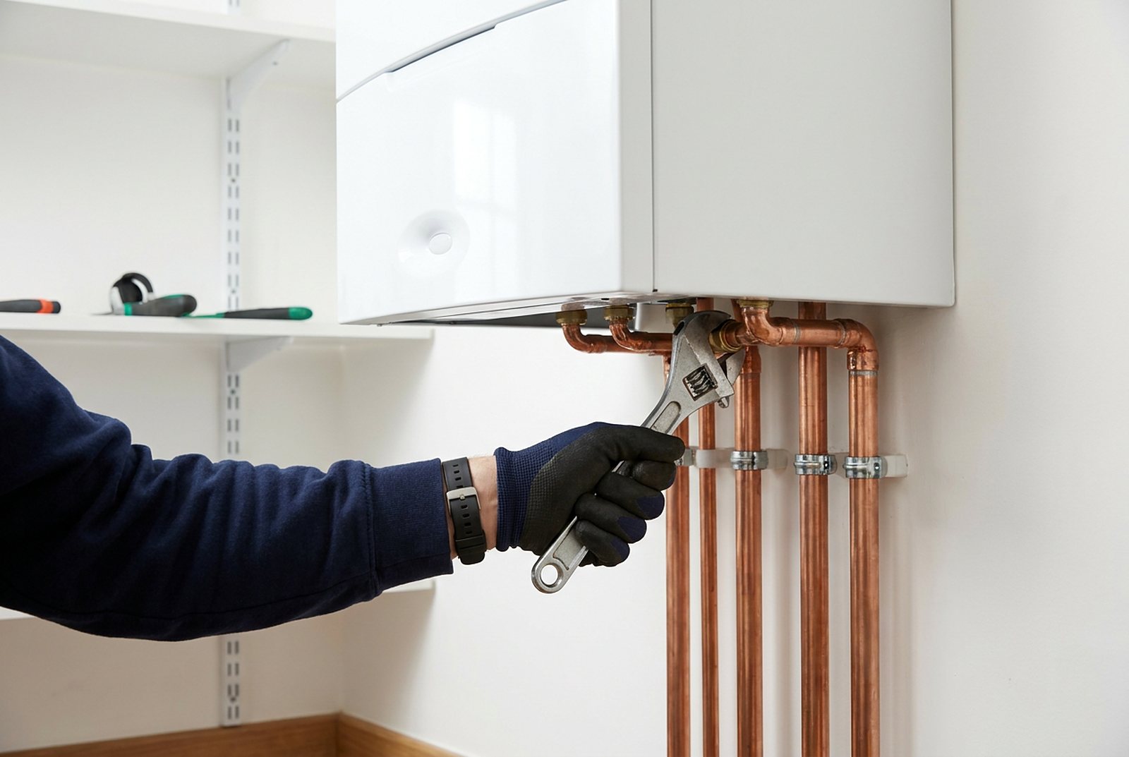 A plumber tightening new copper pipework below a wall-mounted boiler